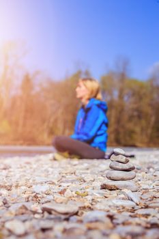 Cairn on a pebble beach, meditating woman in the background. Morning sun.