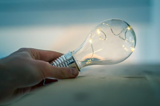 Hands are holding a LED lightbulb over the wooden floor. Symbol for ideas and innovation. Window
