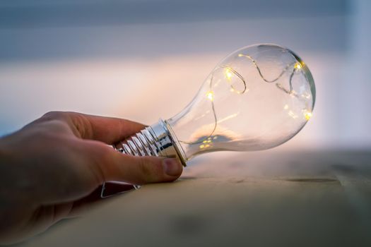 Hands are holding a LED lightbulb over the wooden floor. Symbol for ideas and innovation. Window