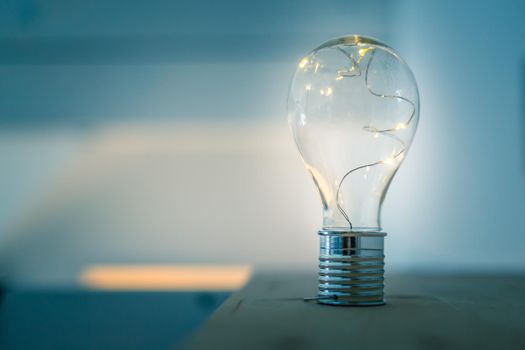 LED light bulb is lying on a wooden table. Symbol for ideas and innovation. Spot lights in the blurry background.