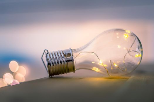 LED light bulb is lying on a wooden table. Symbol for ideas and innovation. Spot lights in the blurry background.