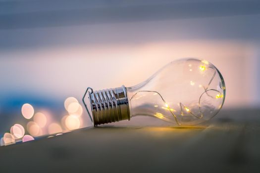 LED light bulb is lying on a wooden table. Symbol for ideas and innovation. Spot lights in the blurry background.
