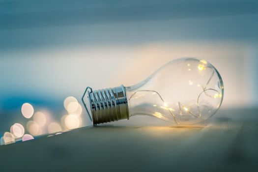 LED light bulb is lying on a wooden table. Symbol for ideas and innovation. Spot lights in the blurry background.