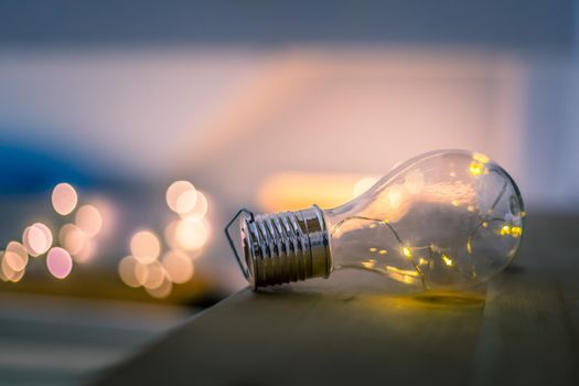 LED light bulb is lying on a wooden table. Symbol for ideas and innovation. Spot lights in the blurry background.