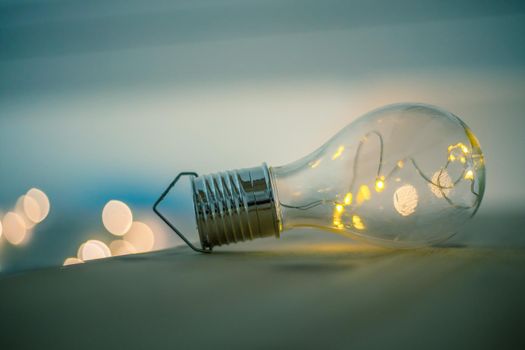 LED light bulb is lying on a wooden table. Symbol for ideas and innovation. Spot lights in the blurry background.