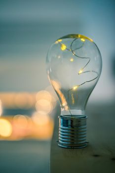 LED light bulb is lying on a wooden table. Symbol for ideas and innovation. Spot lights in the blurry background.