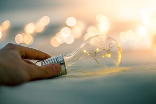LED light bulb is lying in the bed, hands touching. Symbol for ideas and innovation. Spot lights in the blurry background.