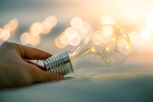 LED light bulb is lying in the bed, hands touching. Symbol for ideas and innovation. Spot lights in the blurry background.