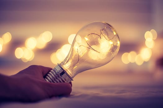 LED light bulb is lying in the bed, hands touching. Symbol for ideas and innovation. Spot lights in the blurry background.