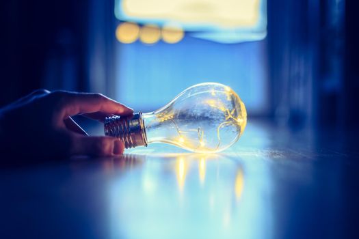 Hands are holding a LED lightbulb over the wooden floor. Symbol for ideas and innovation. Window and light in the blurry background.