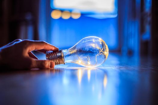 Hands are holding a LED lightbulb over the wooden floor. Symbol for ideas and innovation. Window and light in the blurry background.