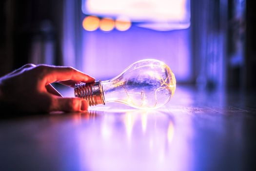 Hands are holding a LED lightbulb over the wooden floor. Symbol for ideas and innovation. Window and light in the blurry background.