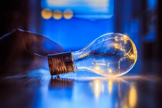 Hands are holding a LED lightbulb over the wooden floor. Symbol for ideas and innovation. Window and light in the blurry background.