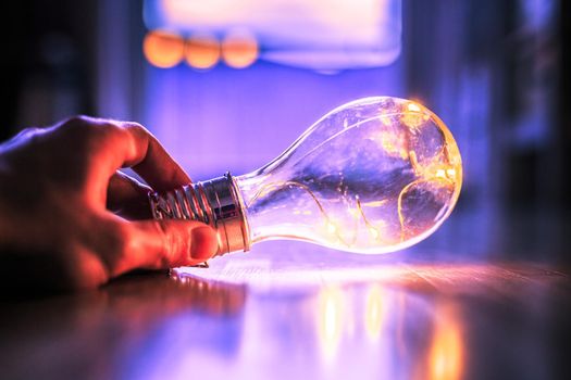 Hands are holding a LED lightbulb over the wooden floor. Symbol for ideas and innovation. Window and light in the blurry background.