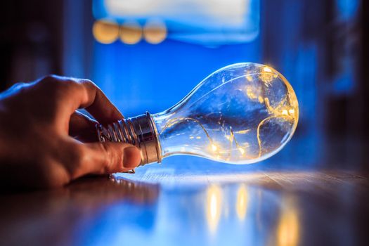 Hands are holding a LED lightbulb over the wooden floor. Symbol for ideas and innovation. Window and light in the blurry background.