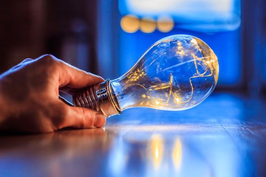 Hands are holding a LED lightbulb over the wooden floor. Symbol for ideas and innovation. Window and light in the blurry background.