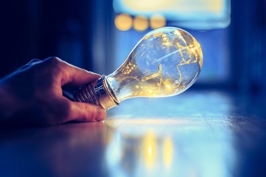 Hands are holding a LED lightbulb over the wooden floor. Symbol for ideas and innovation. Window and light in the blurry background.