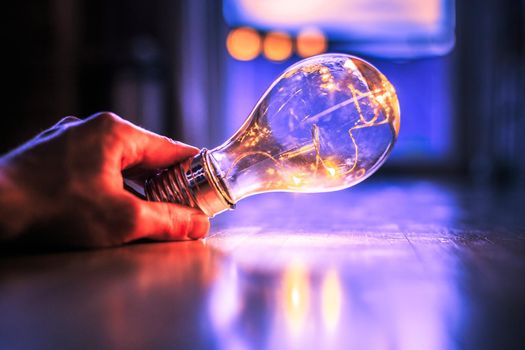Hands are holding a LED lightbulb over the wooden floor. Symbol for ideas and innovation. Window and light in the blurry background.