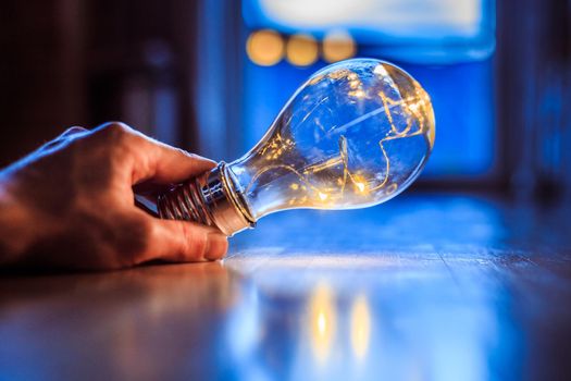 Hands are holding a LED lightbulb over the wooden floor. Symbol for ideas and innovation. Window and light in the blurry background.