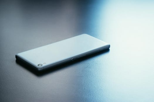 Modern white smart phone is lying on a grey surface or table, perspective view
