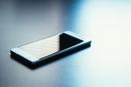 Modern white smart phone is lying on a grey surface or table, perspective view