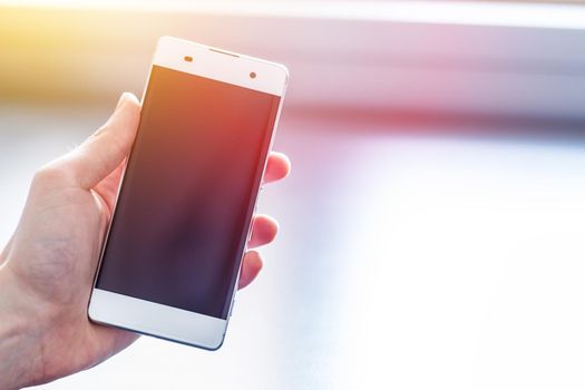 Man is holding a modern smart phone in the hand, grey desk in the background