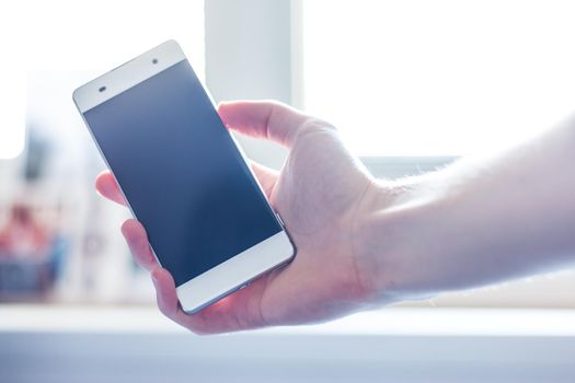 Man is holding a modern smart phone in the hand, grey desk in the background