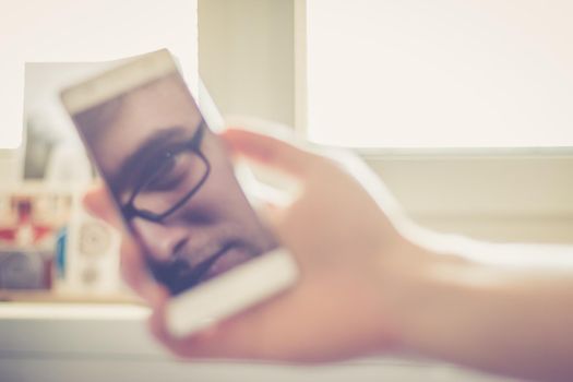 Man holds a smart phone in his hand, reflection of his face on the display