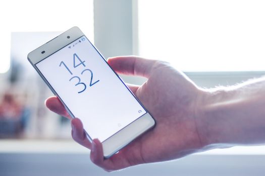 Man is holding a modern smart phone in the hand, grey desk in the background