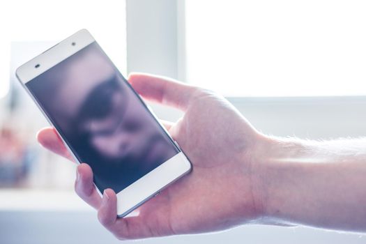 Man holds a smart phone in his hand, reflection of his face on the display