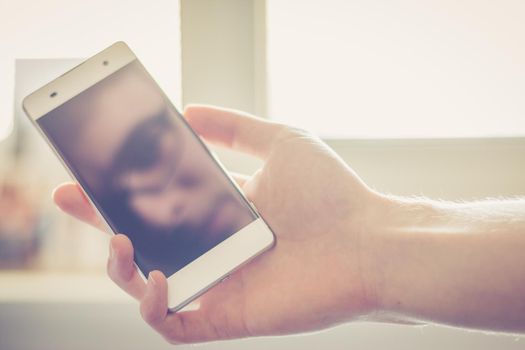 Man holds a smart phone in his hand, reflection of his face on the display