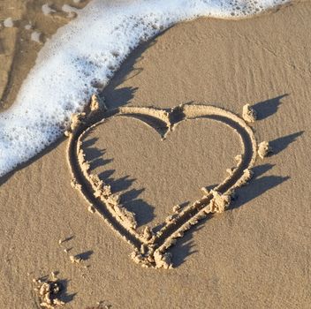 A beautiful heart shape painted into the sand of a baltic sea beach with some water waves