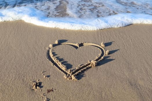 A beautiful heart shape painted into the sand of a baltic sea beach with some water waves