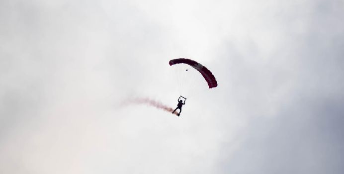 silhouette parachute stunt unfocused and blurry while gliding in the air with red smoke trail during an air exhibition in Singapore