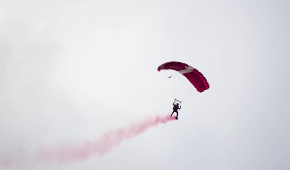 silhouette parachute stunt unfocused and blurry while gliding in the air with red smoke trail during an air exhibition in Singapore