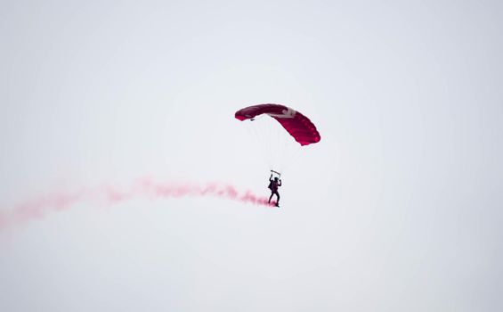 silhouette parachute stunt unfocused and blurry while gliding in the air with red smoke trail during an air exhibition in Singapore