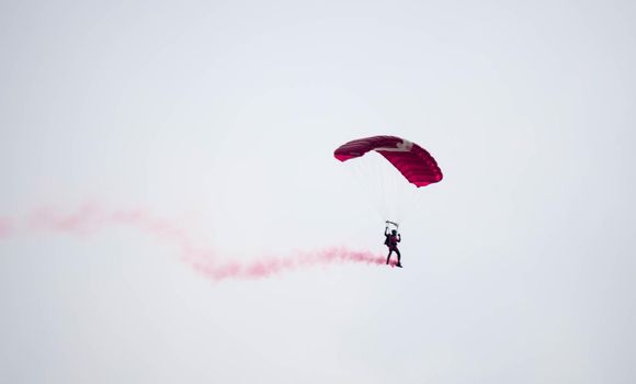 silhouette parachute stunt unfocused and blurry while gliding in the air with red smoke trail during an air exhibition in Singapore