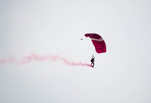 silhouette parachute stunt unfocused and blurry while gliding in the air with red smoke trail during an air exhibition in Singapore