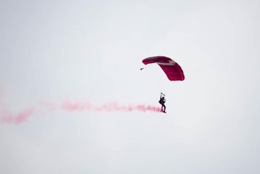 silhouette parachute stunt unfocused and blurry while gliding in the air with red smoke trail during an air exhibition in Singapore