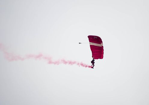 silhouette parachute stunt unfocused and blurry while gliding in the air with red smoke trail during an air exhibition in Singapore