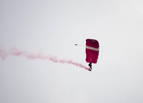 silhouette parachute stunt unfocused and blurry while gliding in the air with red smoke trail during an air exhibition in Singapore