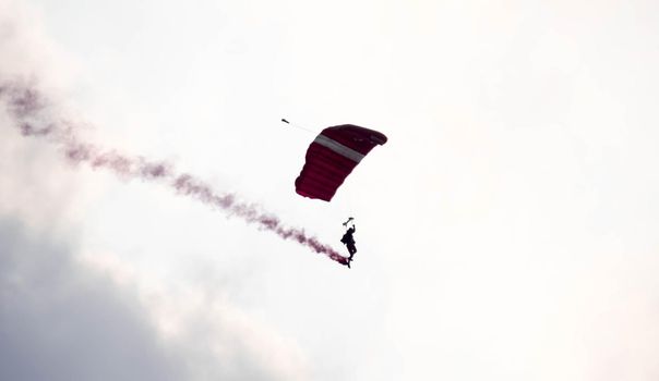 silhouette parachute stunt unfocused and blurry while gliding in the air with red smoke trail during an air exhibition in Singapore