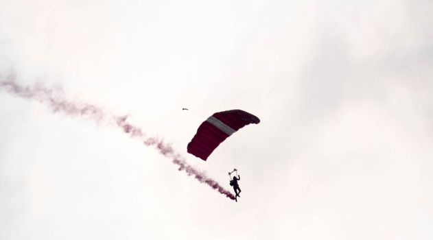 silhouette parachute stunt unfocused and blurry while gliding in the air with red smoke trail during an air exhibition in Singapore