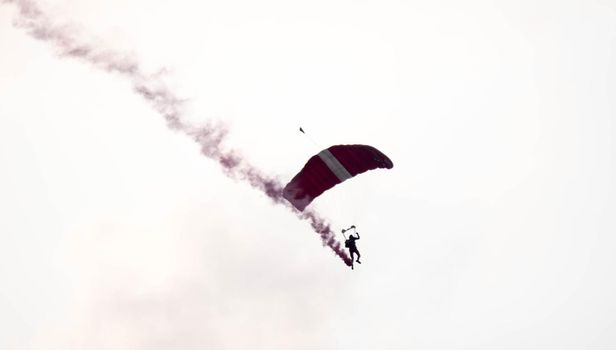 silhouette parachute stunt unfocused and blurry while gliding in the air with red smoke trail during an air exhibition in Singapore