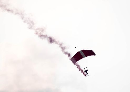 silhouette parachute stunt unfocused and blurry while gliding in the air with red smoke trail during an air exhibition in Singapore