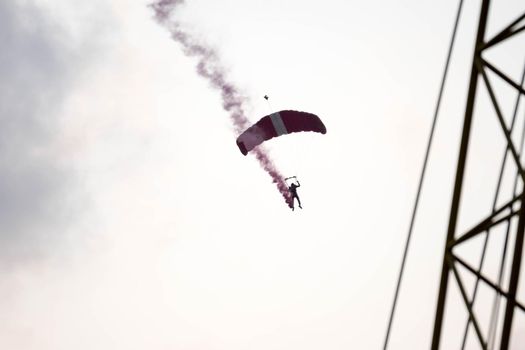 silhouette parachute stunt unfocused and blurry while gliding in the air with red smoke trail during an air exhibition in Singapore