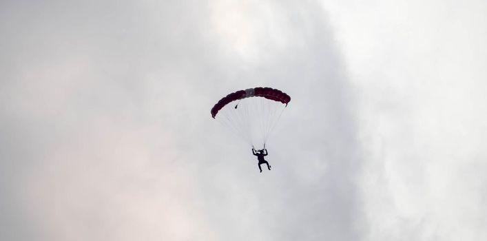 silhouette parachute stunt unfocused and blurry while gliding in the air with red smoke trail during an air exhibition in Singapore