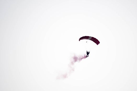 silhouette parachute stunt unfocused and blurry while gliding in the air with red smoke trail during an air exhibition in Singapore