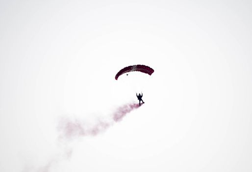 silhouette parachute stunt unfocused and blurry while gliding in the air with red smoke trail during an air exhibition in Singapore