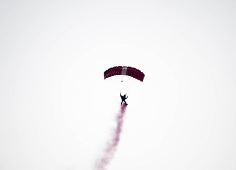 silhouette parachute stunt unfocused and blurry while gliding in the air with red smoke trail during an air exhibition in Singapore